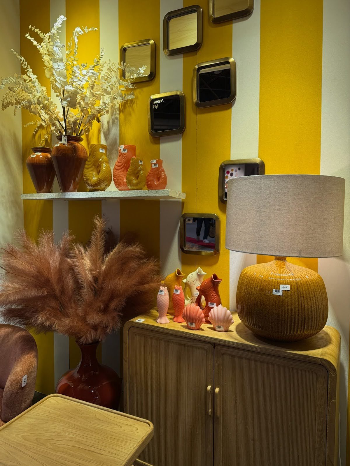 Colorful home decor display with vases, fish figurines, mirrors, and a table lamp against a yellow striped wall.