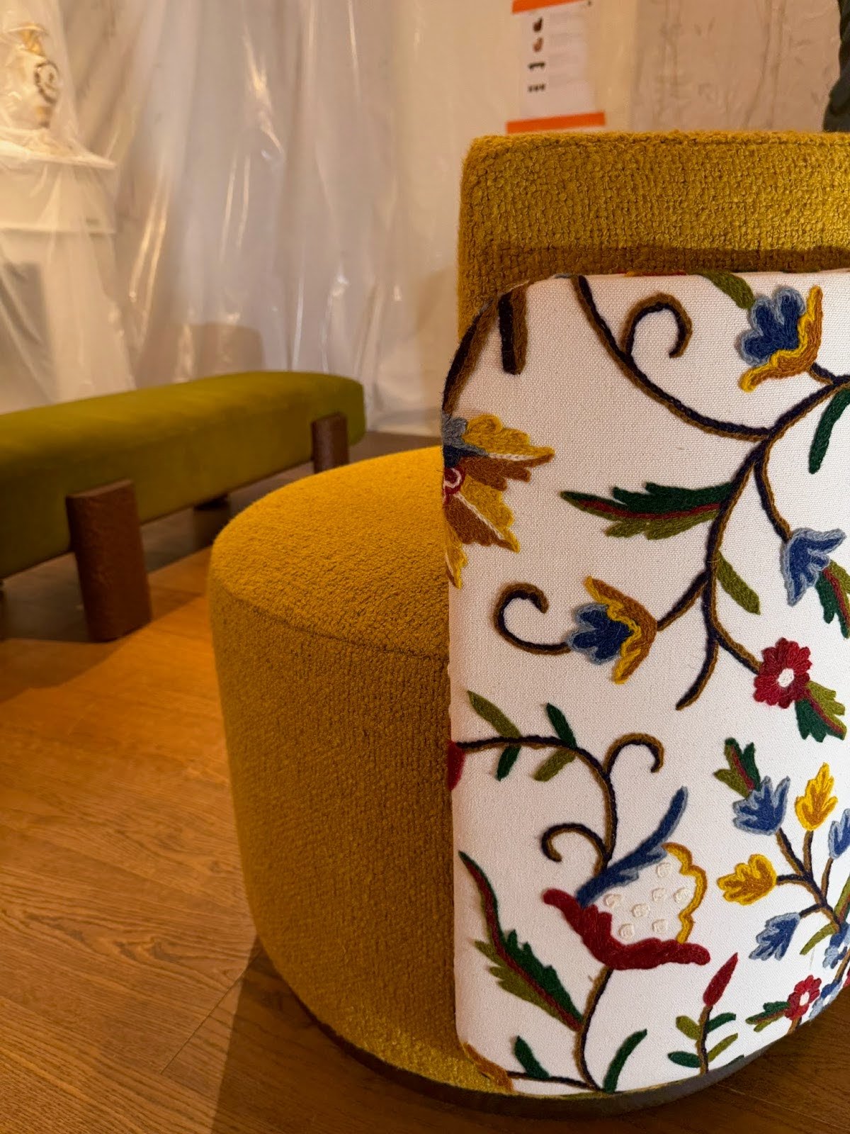Close-up of a mustard yellow upholstered chair with a floral embroidered back panel