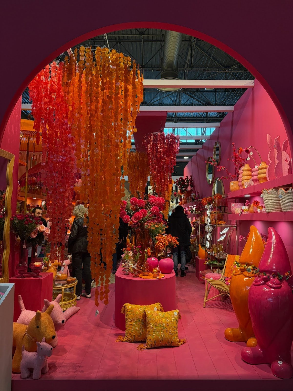 Vibrant pink and orange home decor display with hanging installations, flowers, and colorful accessories