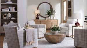 Bright modern living room with four armchairs, a round coffee table, wood console, lamps, plants, and a large round mirror