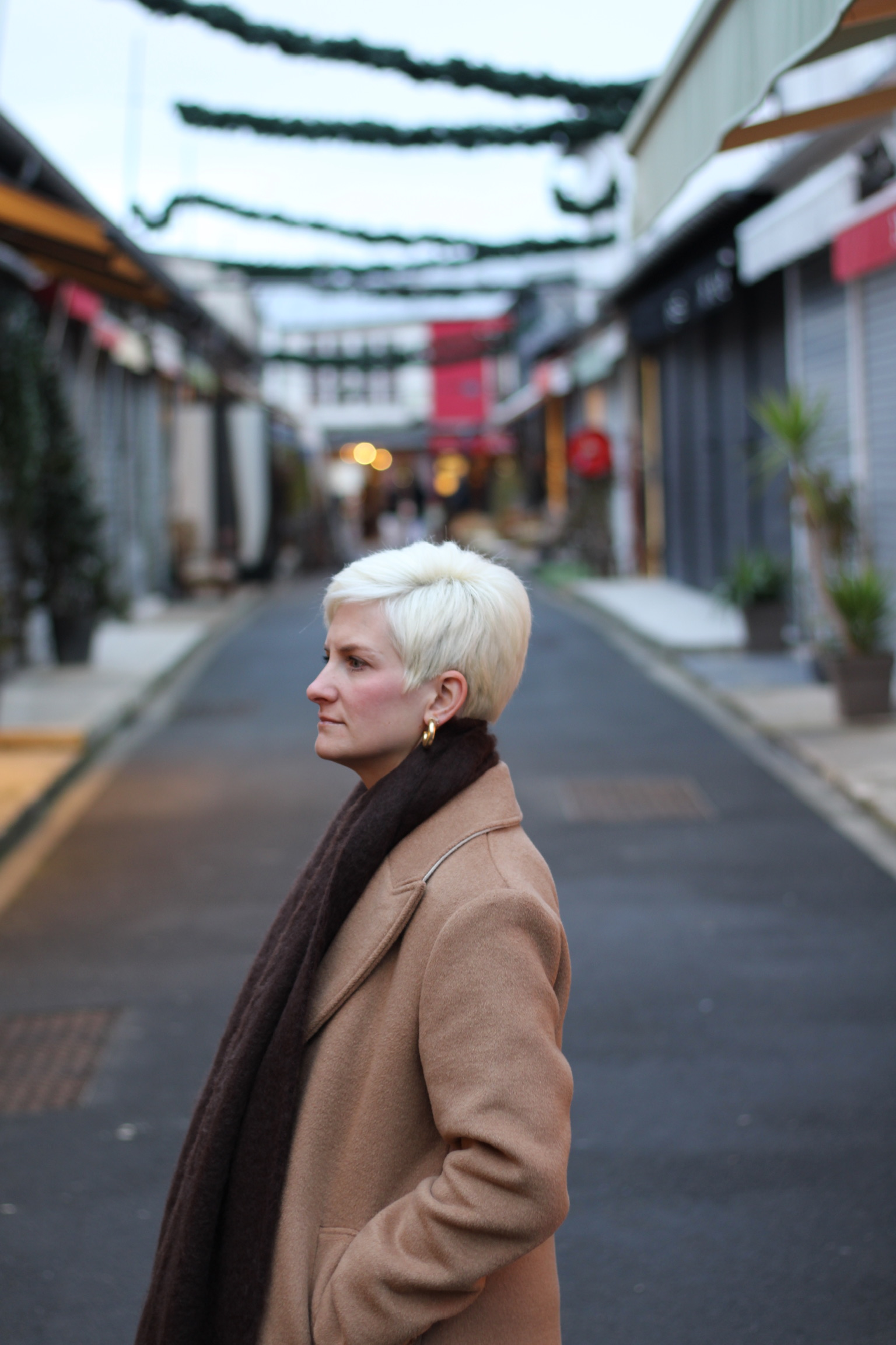 Woman standing in profile on a quiet shopping street lined with storefronts