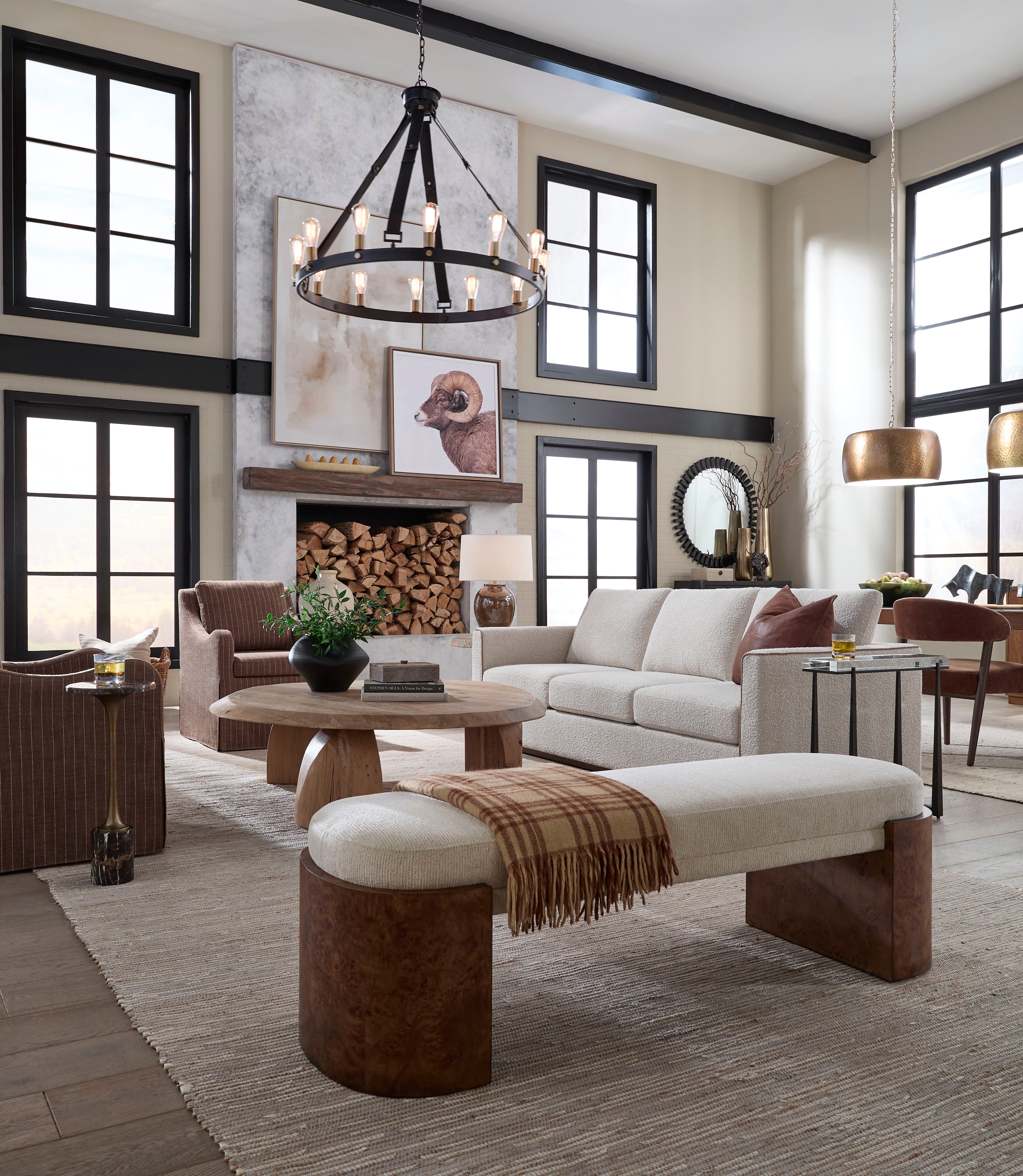 Modern rustic living room with a large black chandelier, ligh sofa, wood accents, and a fireplace stacked with logs.