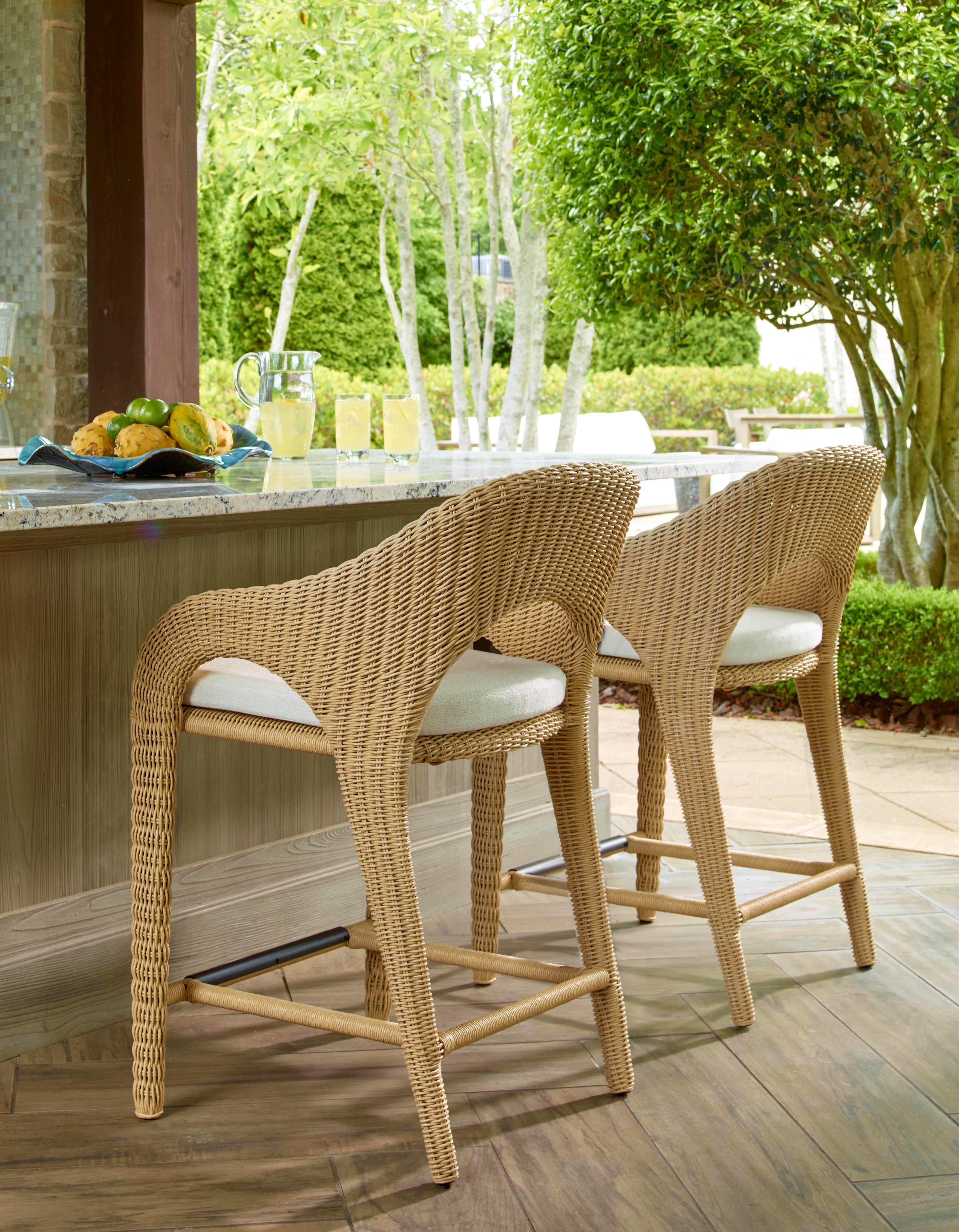 Two woven outdoor bar stools at a patio counter with drinks and fruit nearby