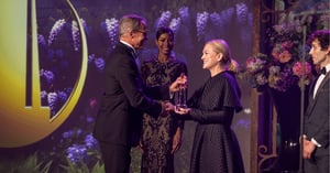 Man suit receiving an award from women in black dress on a stage