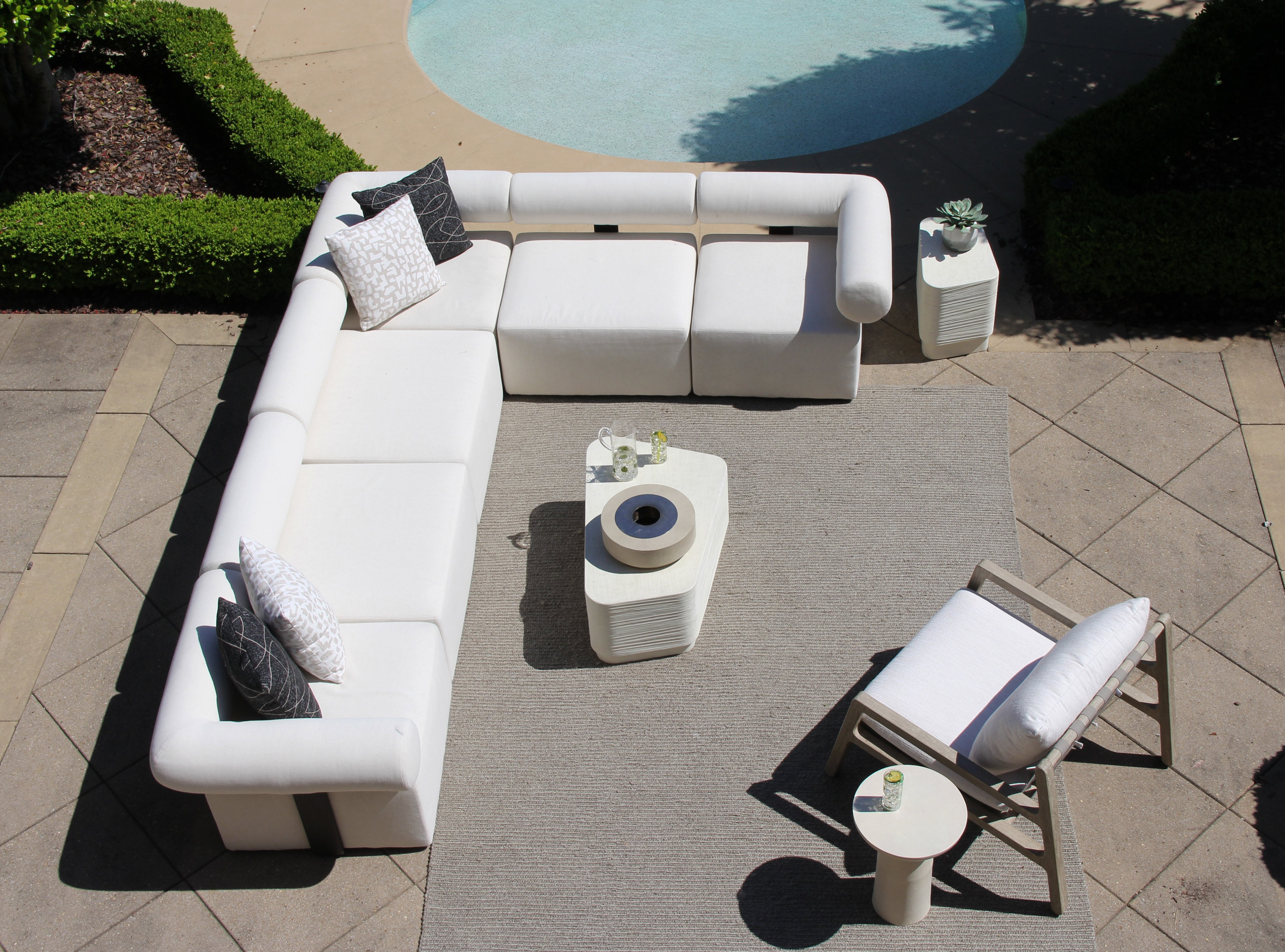 Outdoor patio seating area with a white sectional sofa, lounge chair, and coffee table beside a swimming pool