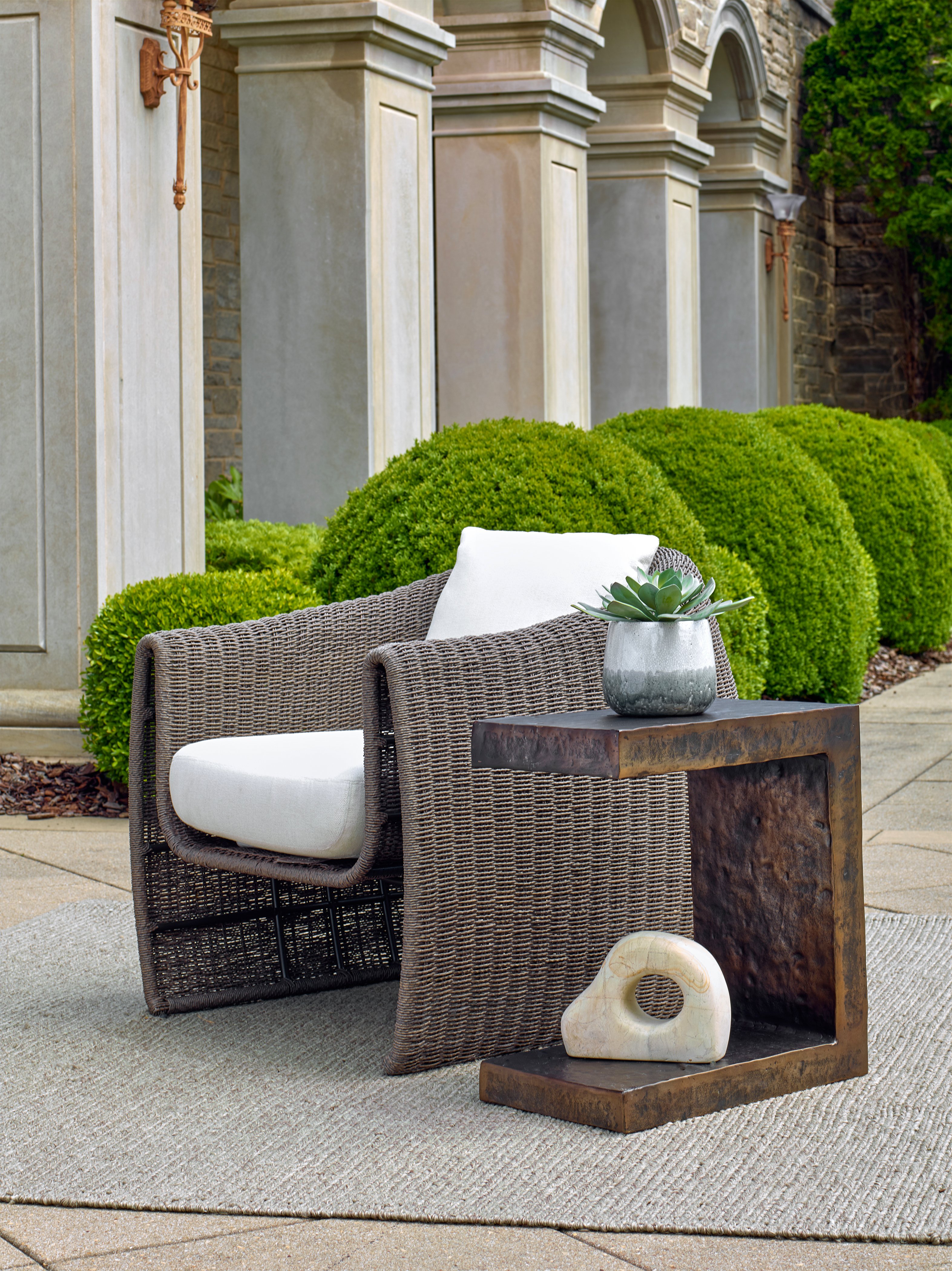 Woven outdoor lounge chair with a white cushion beside a rustic metal side table on a patio