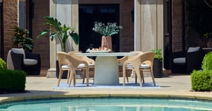 Four woven chairs around a white table by a pool