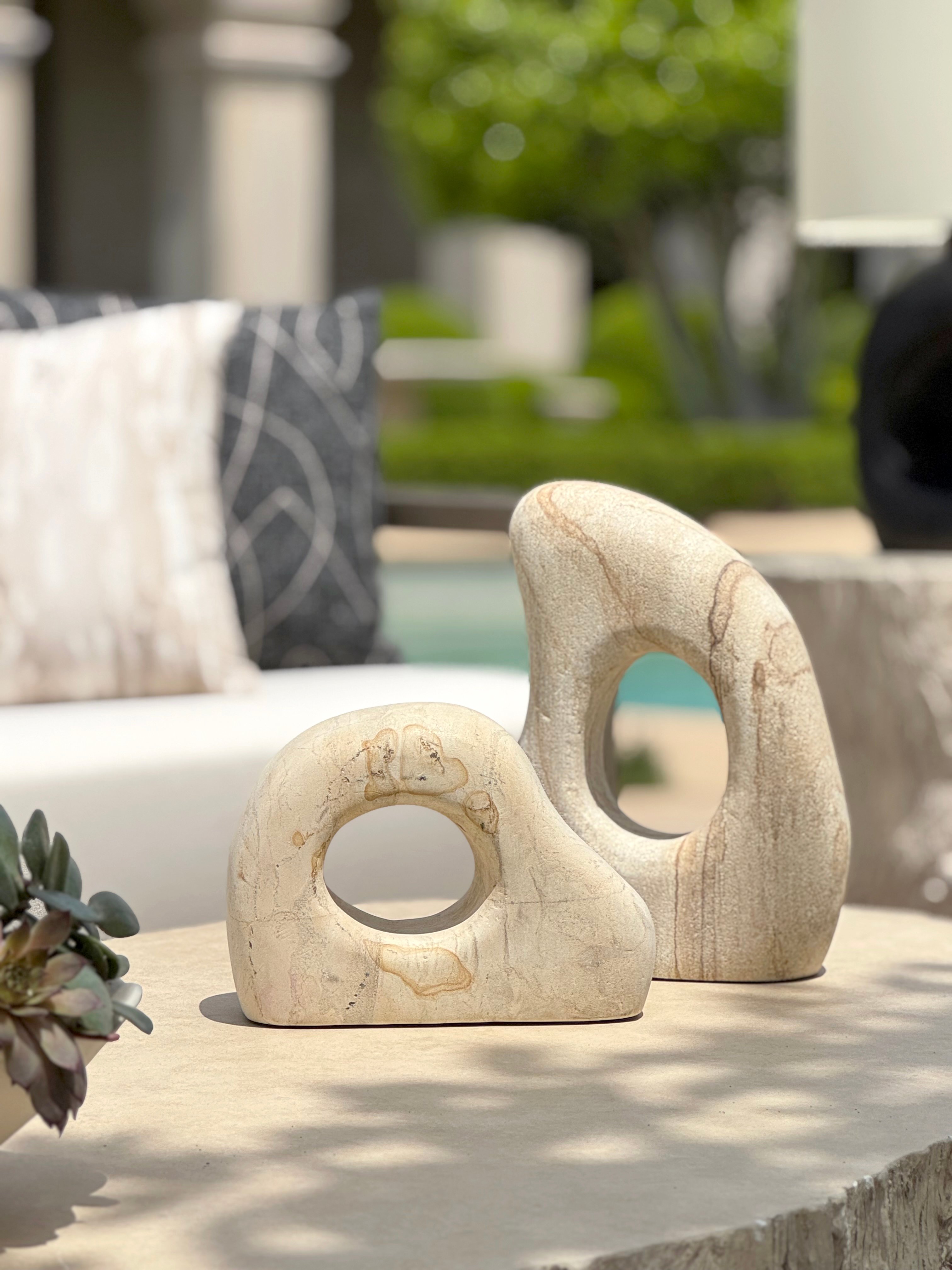 Two abstract stone sculptures with circular cutouts displayed on an outdoor table