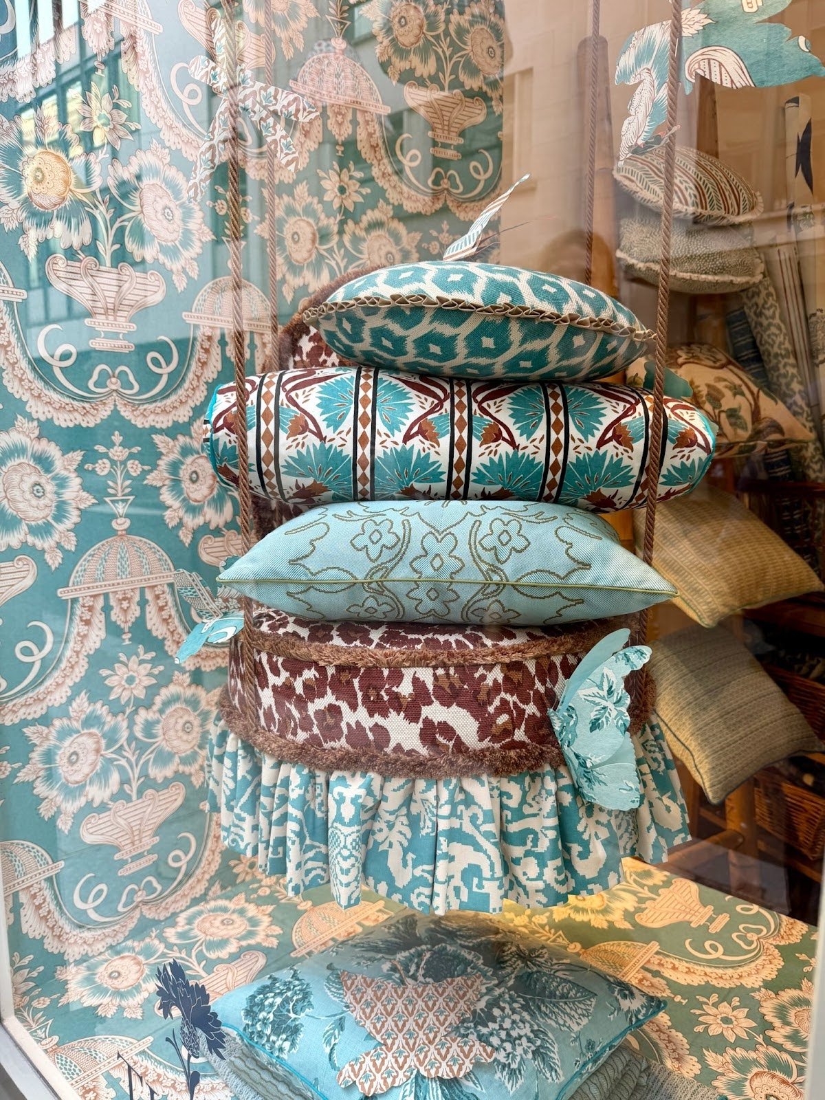 stacked decorative pillows with teal and brown patterns displayed against patterned wallpaper