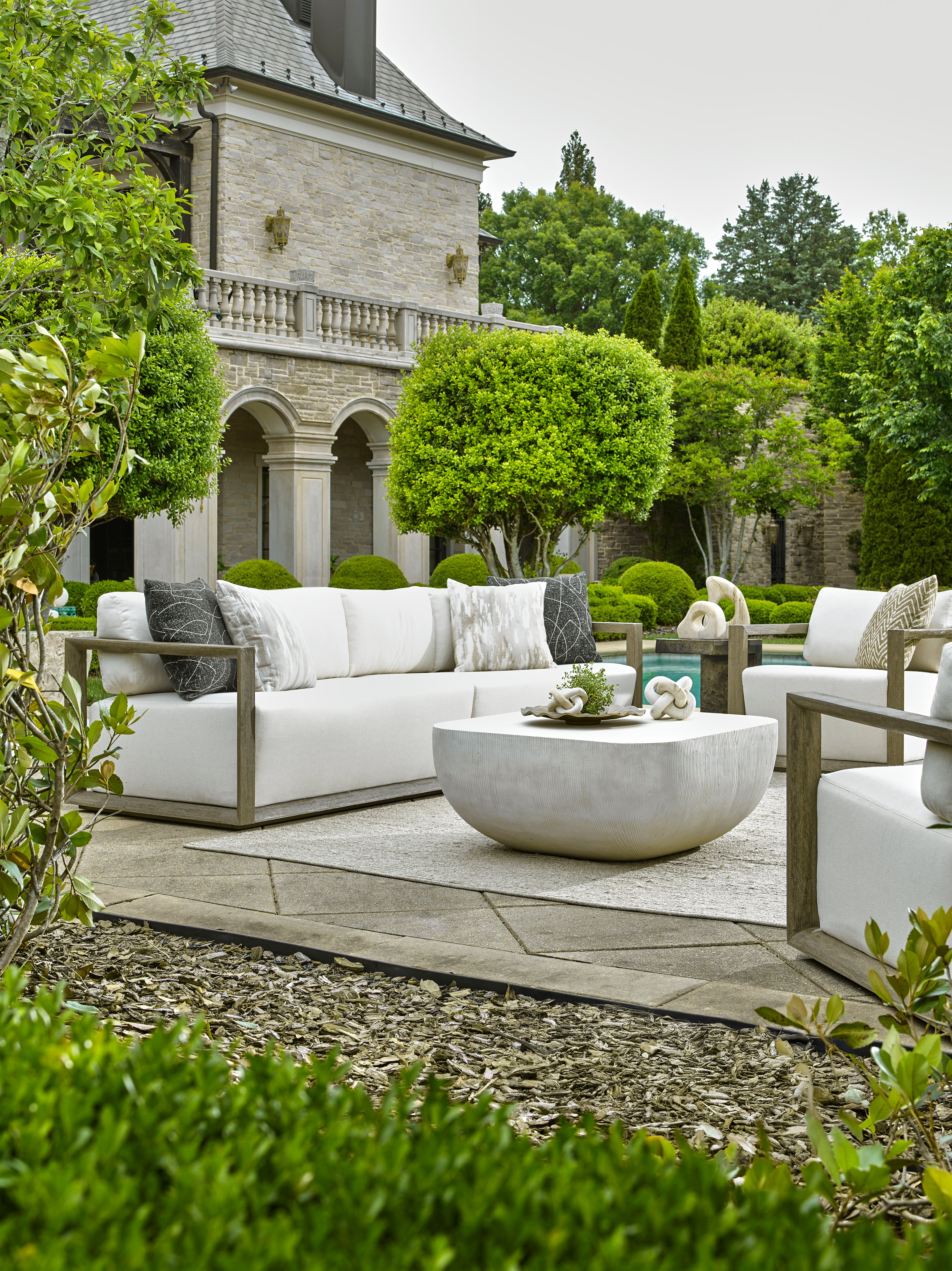 Outdoor seating area with a white sofa and round coffee table in a landsccaped graden 