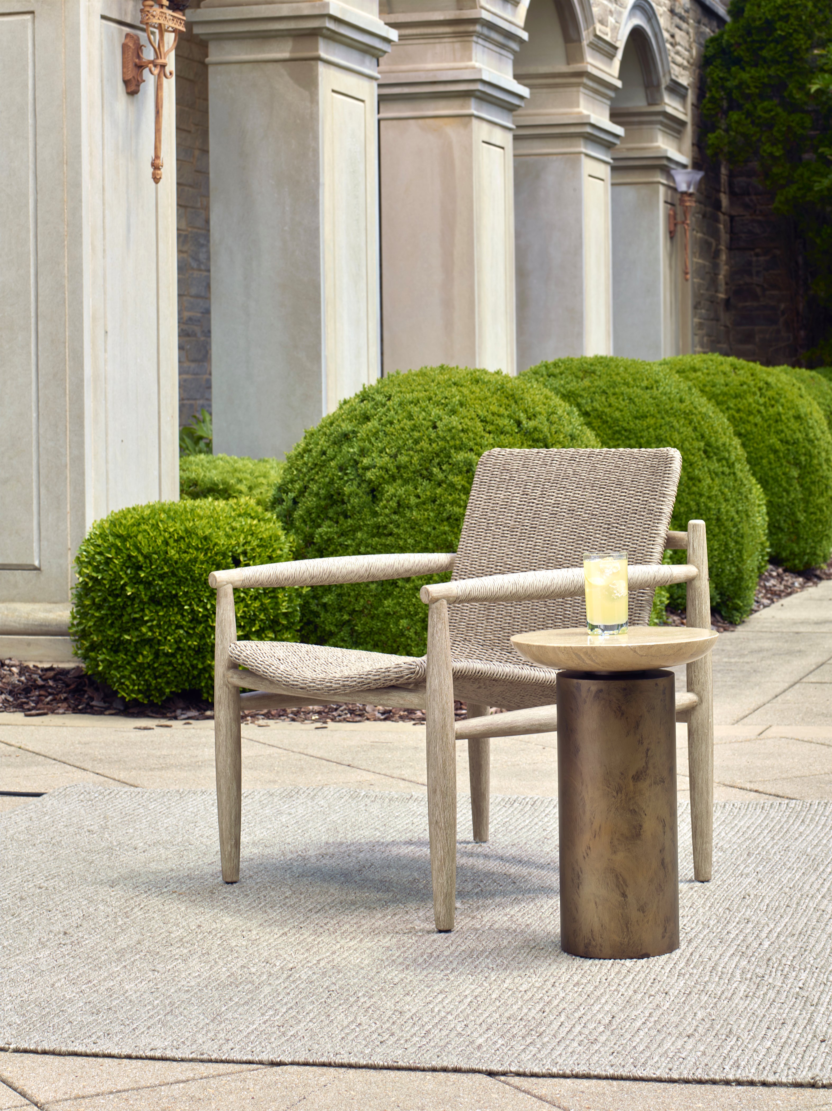 Woven outdoor chair with wooden frame beside a small round side table with a drink